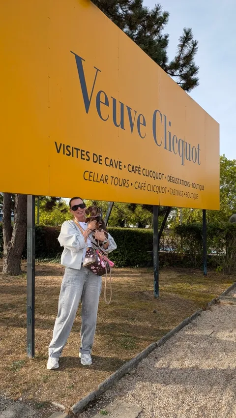 Celine in de armen van haar baasje voor het gele bord van Veuve Clicquot in Reims