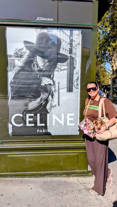 Haar baasje met Celine in de tas naast een CELINE-poster in Parijs