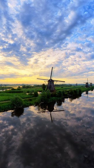 Luchtbeeld van een Nederlandse molen bij het water tijdens zonsondergang