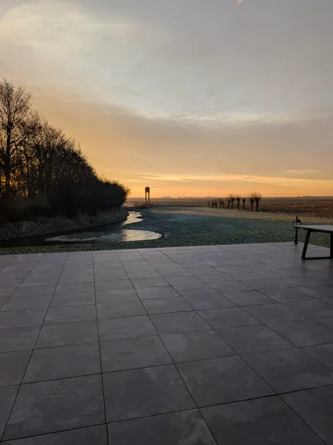 Zonsopkomst boven de polder met vorst op het gras, gezien vanaf het terras